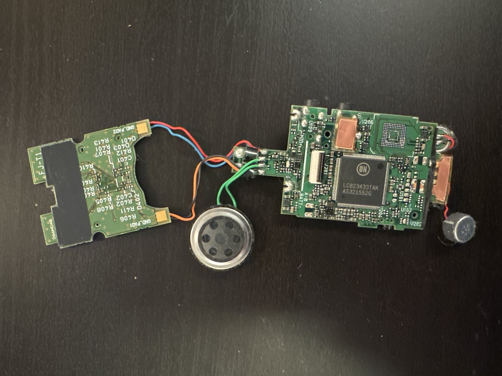 Disassembled Olympus voice recorder circuit boards, speaker, microphone and controller chip laid out on a bench