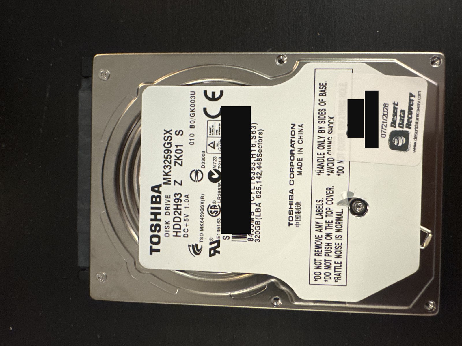 Toshiba MK3259GSX 320 GB laptop hard drive label with serial number and barcode redacted, and the intake sticker case number and client name blacked out