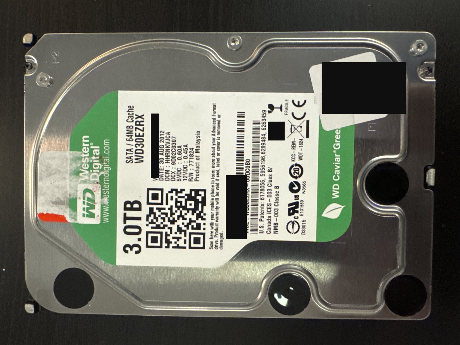 Western Digital WD30EZRX 3 TB SATA hard drive label with serial number, WWN, barcode and data-matrix redacted, and the intake sticker covered